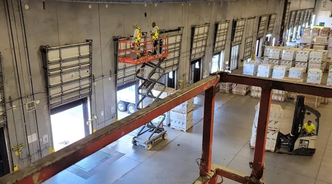 Operatives cleaning a large industrial warehouse from a scissor lift