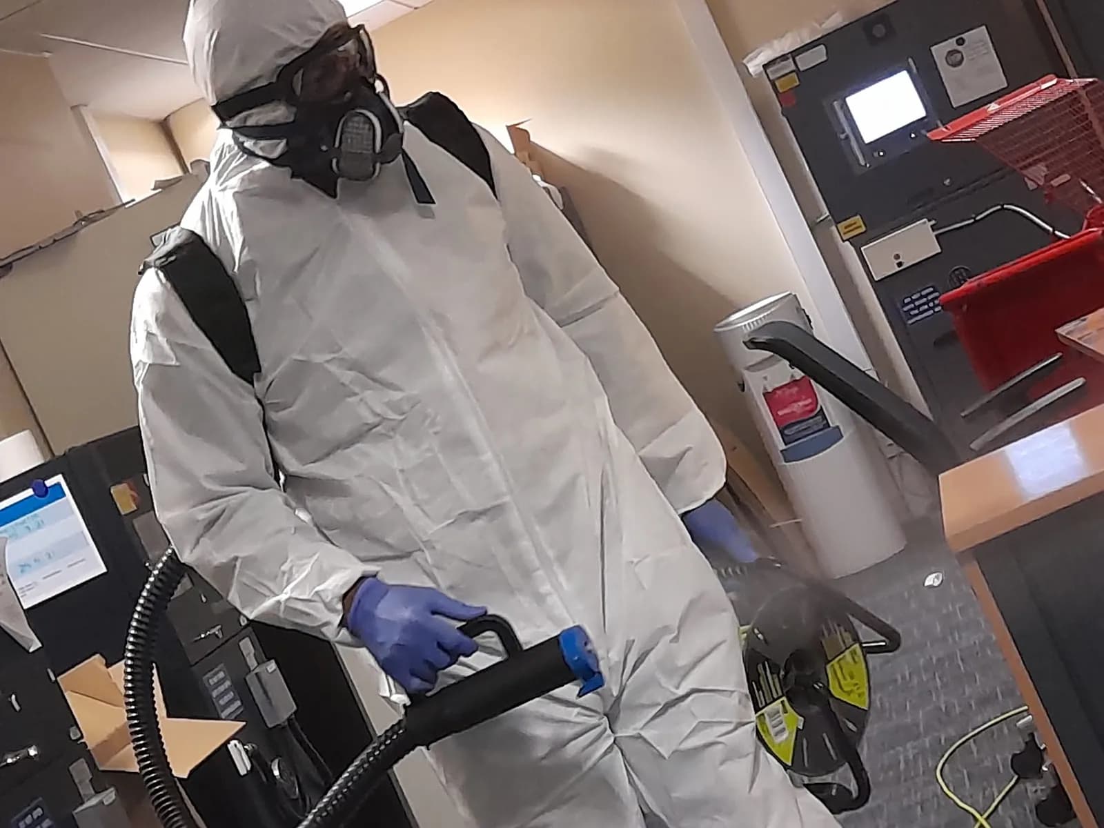 Operative in a hazmat suit, respirator and gloves using decontamination equipment